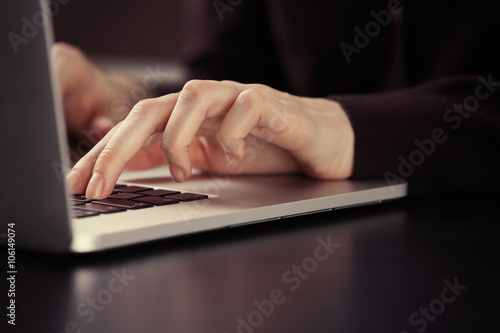Female hands using laptop on dark wooden table, close up