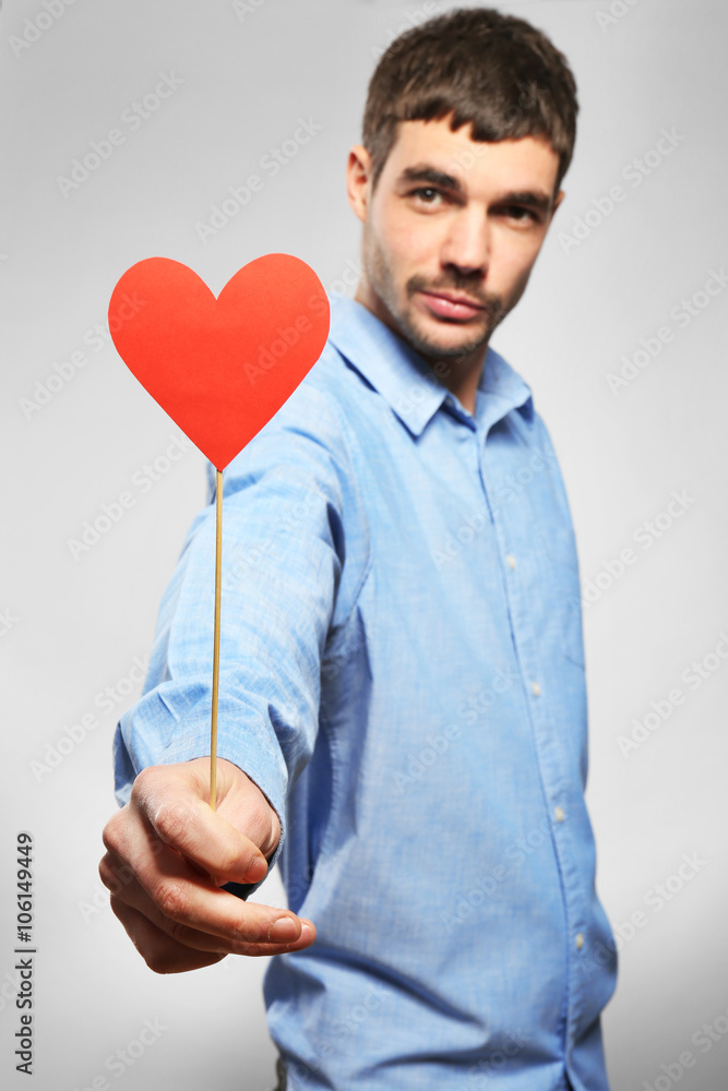 Young man holding red paper heart on grey background Young man holding red paper heart on grey background