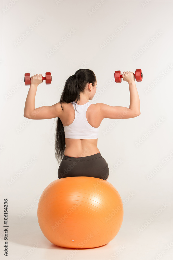 Young sportswoman doing fitness exercise with dumbbells on pilates ball Young sportswoman doing fitness exercise with dumbbells on pilates ball