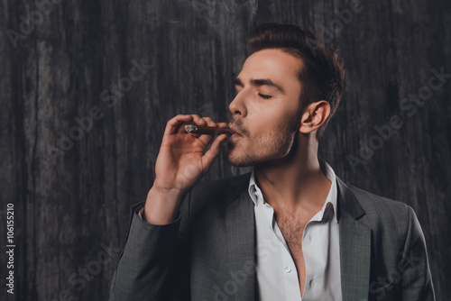 Handome brutal man in suit on the gray background smoking a ciga photo