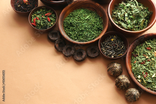 Variety of dry tea in bowls on light brown background, closeup