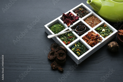 Variety of dry tea in box with green teapot on dark wooden background, closeup