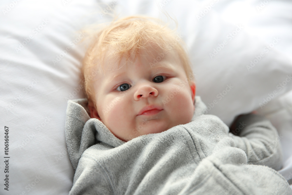 Little baby boy in grey pajamas lying on the bed, close up Little baby boy in grey pajamas lying on the bed, close up
