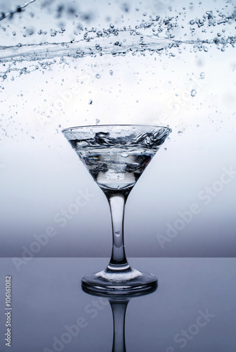 Ice in glass, water splash on table with refllection photo