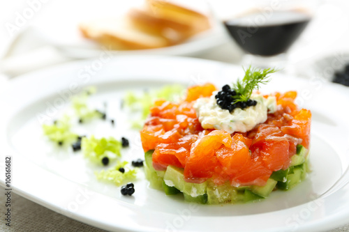Fresh tartar with salmon, cucumber and black caviar on white plate, close up