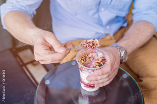 Man eating granola breakfast from a plastic cup with morning light breaking through photo