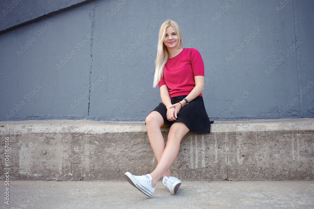 Young happy beautiful blonde woman sitting on the concrete river pier and looking into camera Young happy beautiful blonde woman sitting on the concrete river pier and looking into camera