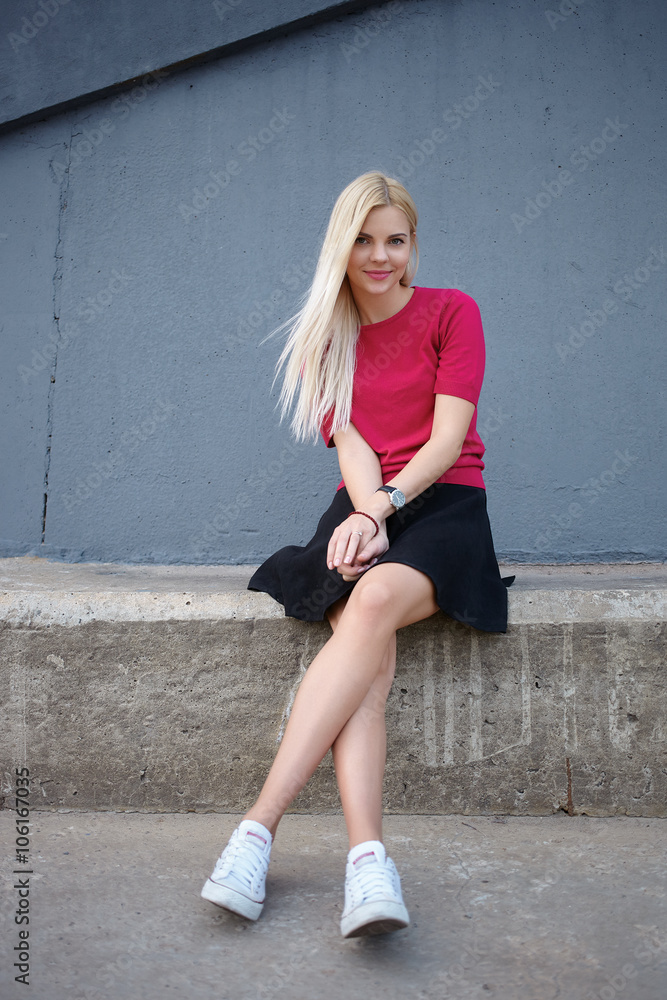Young happy beautiful blonde woman sitting on the concrete river pier and looking into camera Young happy beautiful blonde woman sitting on the concrete river pier and looking into camera