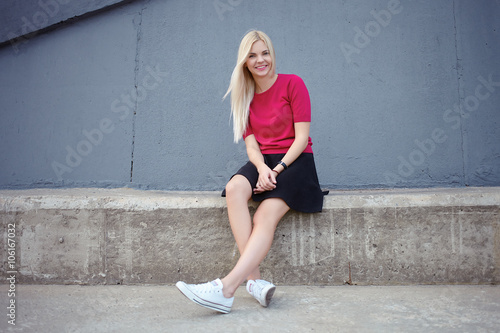 Young happy beautiful blonde woman sitting on the concrete river pier and looking into camera © sergeyzapotylok