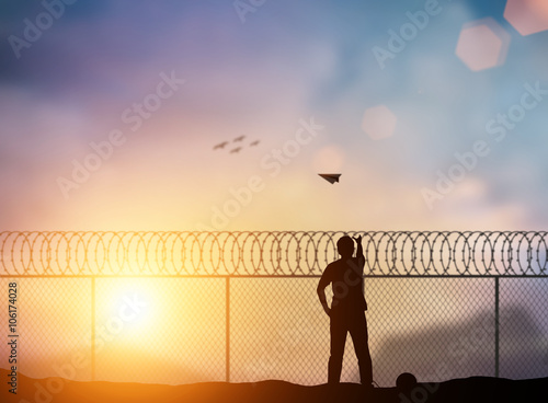 Silhouette of a prisoner behind a barbed wire fence, throw paper airplanes to fight outside the barbed wire fence over blurred nature. Concept Freedom, independent business, independent thinking.