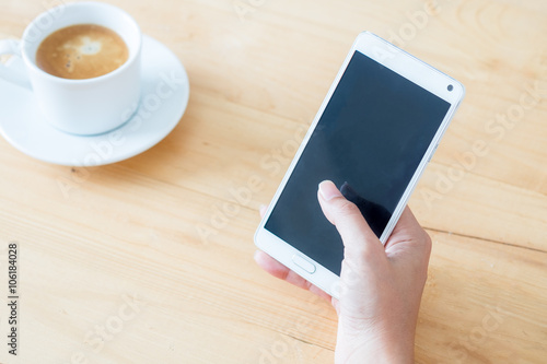 Hand holding phone on wood table and coffee