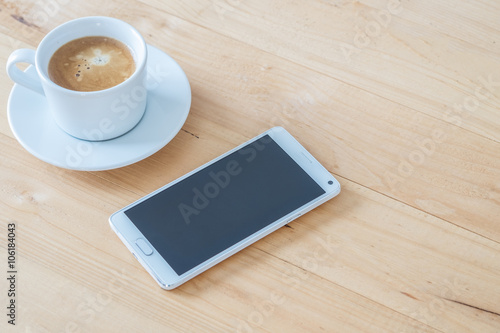 Coffee cup and smartphone on wooden table.