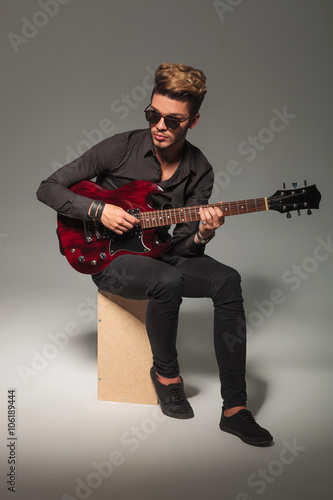 young guitarist sitting on wooden box