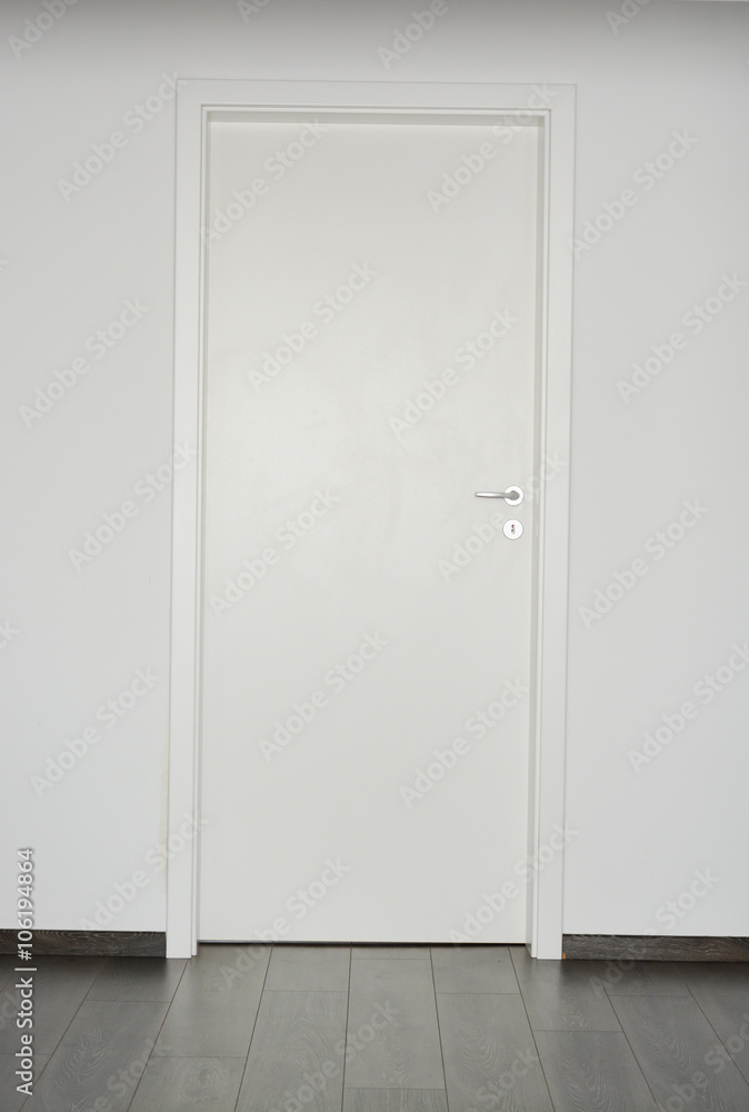 White closed door with silver doorknob on white wall background and parquet floor White closed door with silver doorknob on white wall background and parquet floor