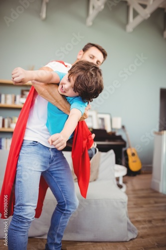Father holding cheerful son wearing superhero costume