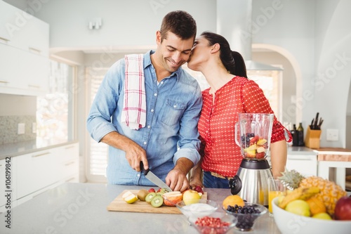 Woman kissing man preparing fruit juice