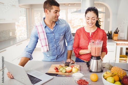 Couple standing with fruit juice while using laptop