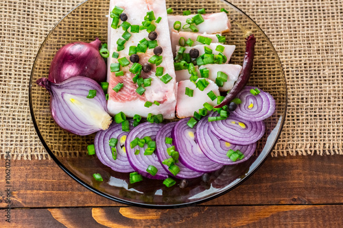 Fresh pork fat, with red hot chili peppers, green and purple onions and  peas allspice beautifully laid out on a glass plate on the background of old boards photo