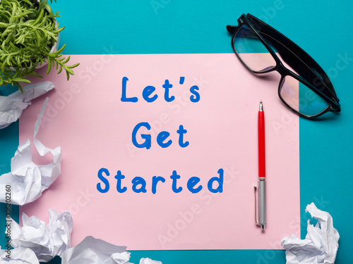 Let's get started message - Office desk table with supplies top view.  crumled paper, pen, glasses and flower. photo