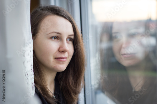 Beatiful young girl watching out of the window; looking from the