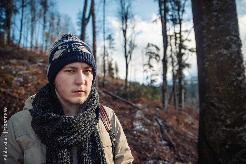 young guy in a warm cap and a jacket with a scarf on the neck, trousers and rubber boots walks alone in the Carpathian mountains with a camera, a tripod and a backpack on his shoulders young guy in a warm cap and a jacket with a scarf on the neck, trousers and rubber boots walks alone in the Carpathian mountains with a camera, a tripod and a backpack on his shoulders