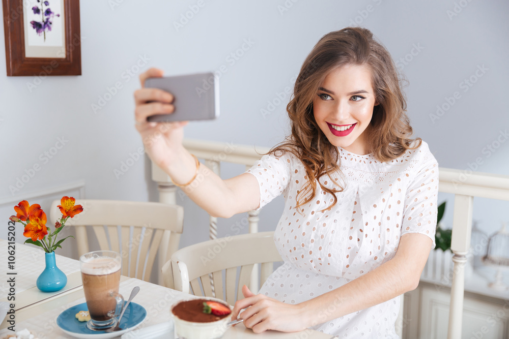 Smiling beautiful woman taking selfie with smartphone sitting in cafe Smiling beautiful woman taking selfie with smartphone sitting in cafe