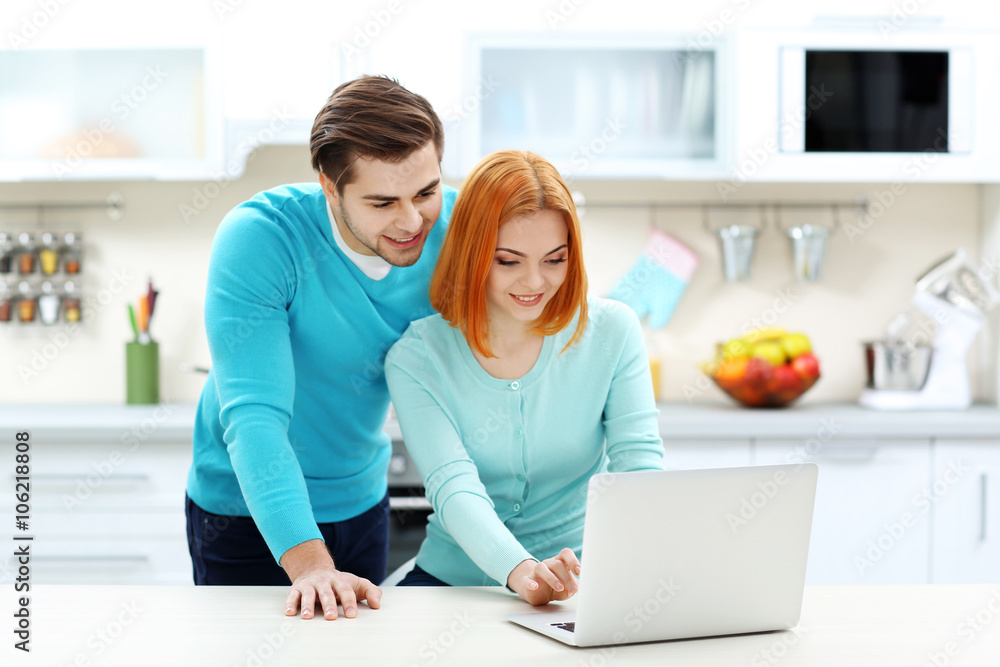 Young couple using laptop on the kitchen Young couple using laptop on the kitchen