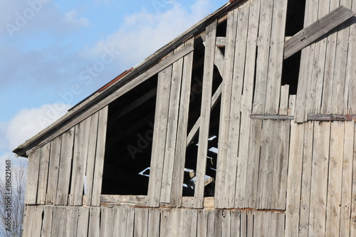 Old weathered barn, missing boards, faded and cracked, turning gray with age, still attached to barn. 