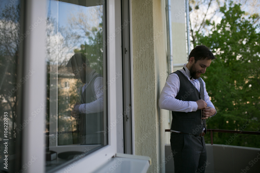 Stylish and handsome groom in waistcoat tying his bow-tie in the morning of the wedding day. Groom with beard Stylish and handsome groom in waistcoat tying his bow-tie in the morning of the wedding day. Groom with beard