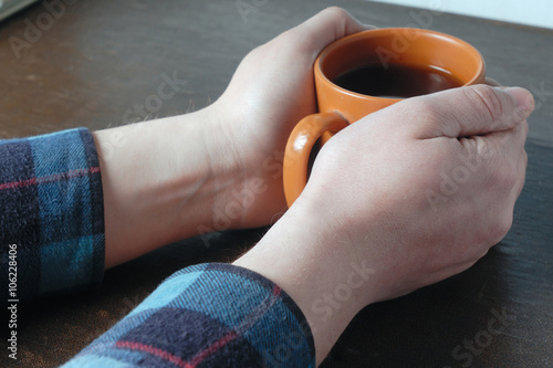 Males hand holding orange cup of tea