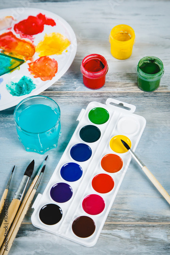 Set of watercolor paints, brushes for painting and palette on old vintage wooden background top view