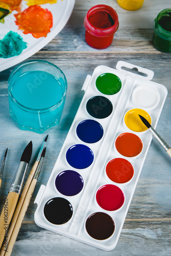 Set of watercolor paints, brushes for painting and palette on old vintage wooden background top view
