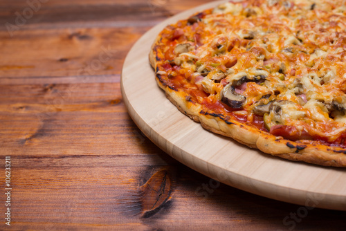 Italian pizza with ham and mushrooms on a wooden board on natural wooden table