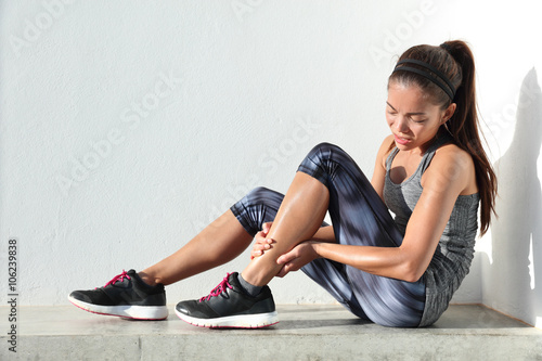 Fototapeta Naklejka Na Ścianę i Meble -  Running injury leg accident- sport woman runner hurting holding painful sprained ankle in pain. Female athlete with joint or muscle soreness and problem feeling ache in her lower body.