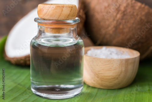 coconut oil in a bottle, background is a half of coconut on a banana leaf