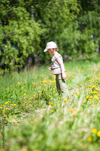 Girl standing on the forest path, looking at dandelions