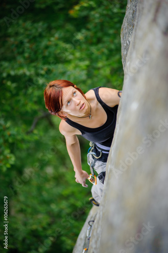 Top view of red-haired athletic female climbing steep cliff wall in summer time. Sport and Healthy lifestyle concept.