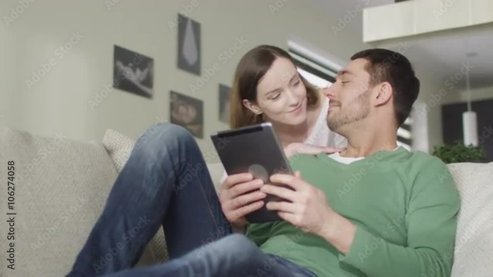 Happy couple is sitting on a sofa at home and using a tablet computer. Shot on RED Cinema Camera. Happy couple is sitting on a sofa at home and using a tablet computer. Shot on RED Cinema Camera.