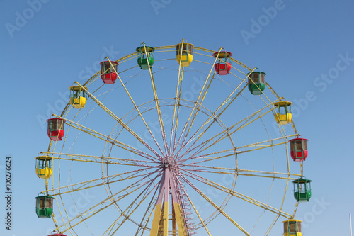 Ferris wheel with color cabins against the blue sky