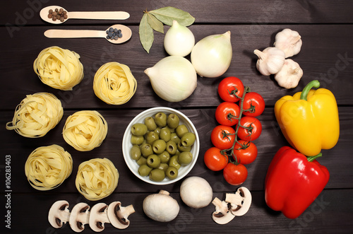 A set of ingredients for cooking pasta for Italian recipe: spaghetti, mushrooms, tomatoes, onions, garlic, pepper, spices, olives on background black rustic table