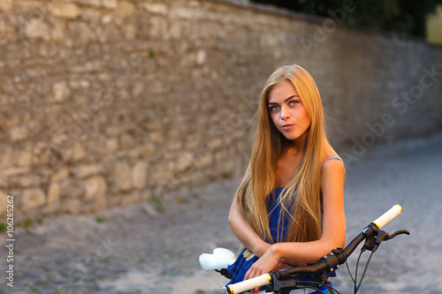 Young cute lady posing with bike near the wall © Aleksey