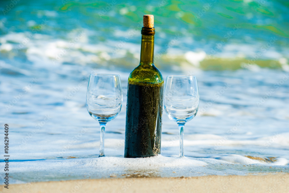 Romantic picnic with glasses of red wine sitting on the beach at the summer sunny day. Waves and sea on the background Romantic picnic with glasses of red wine sitting on the beach at the summer sunny day. Waves and sea on the background