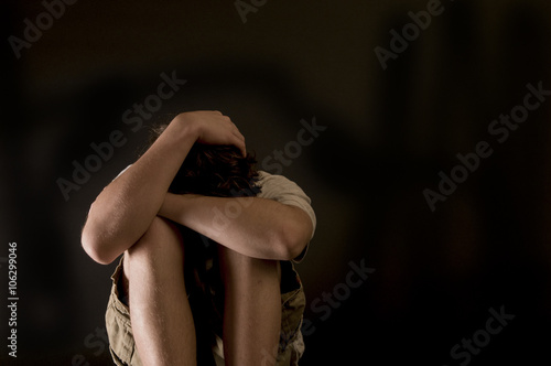 Lonely, hurt teenage boy sitting, arms around knees