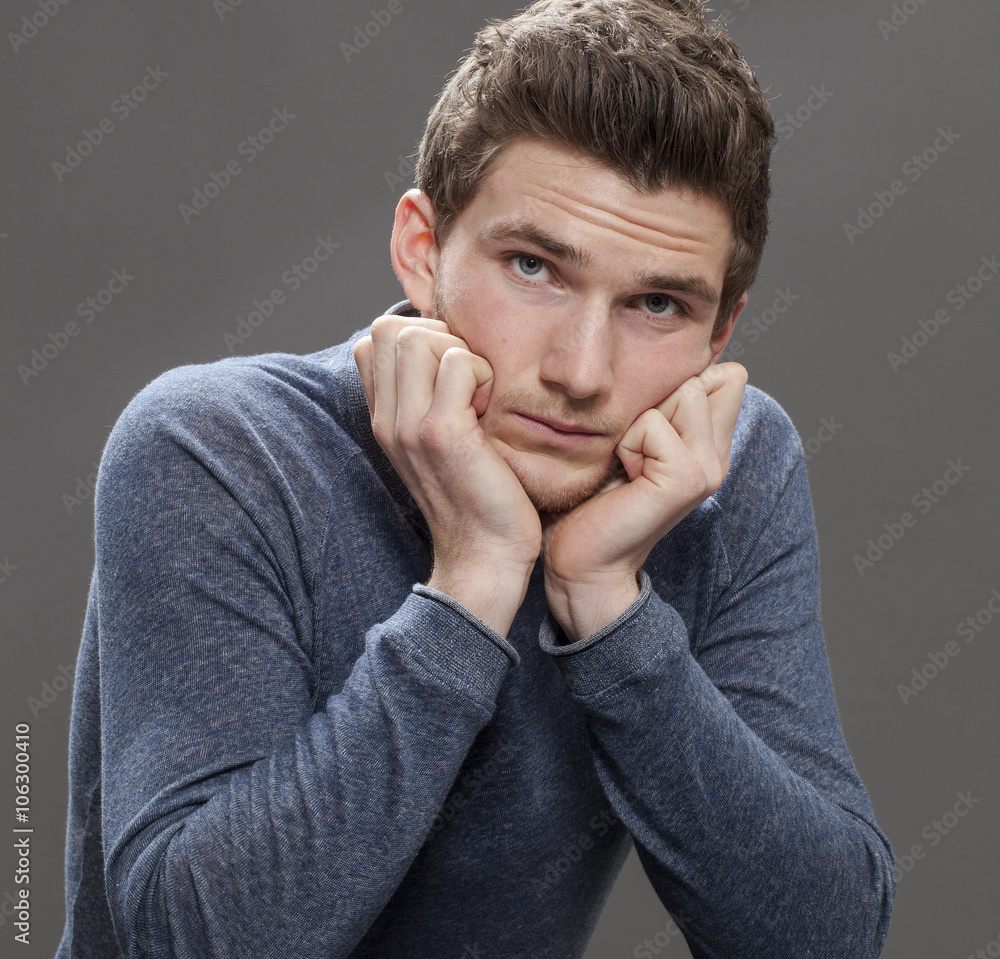 boredom concept - bored male teenager thinking with face leaning on his hands for reflection, gray background.