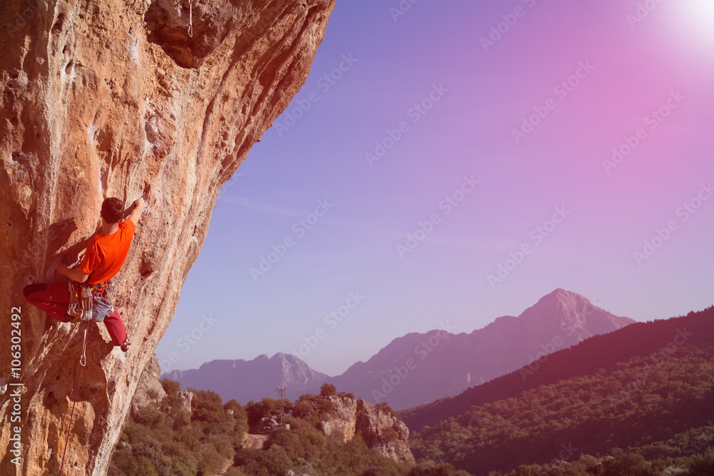 Young male climber hanging by a cliff.