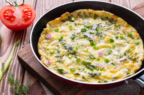pan with a delicious omelette on a cutting board on a wooden background with vegetables