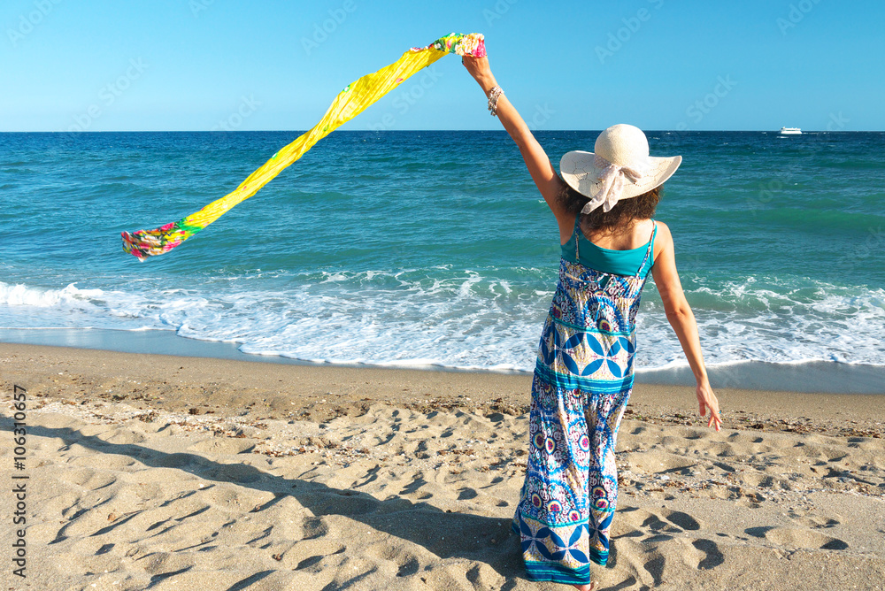 Φωτογραφία Woman standing on the beach (rear view) facing the sea wearing a long dress and a straw hat