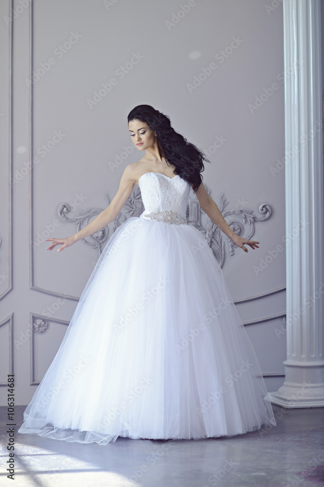 Fototapeta premium Beauty bride in bridal gown indoors. Beautiful model girl in a white wedding dress. Female portrait of cute lady. Woman with hairstyle