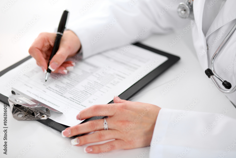Close-up of a female doctor filling out application form , sitting at the table in the hospital Close-up of a female doctor filling out application form , sitting at the table in the hospital