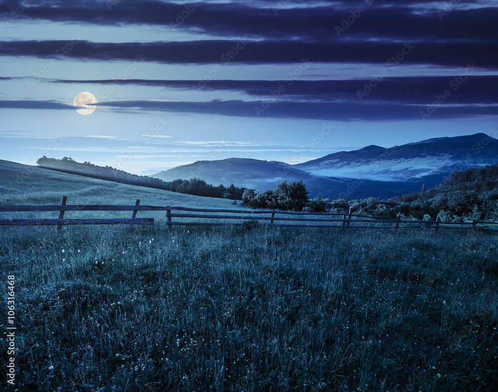 Obraz premium fence on hillside meadow in mountain at sunrise